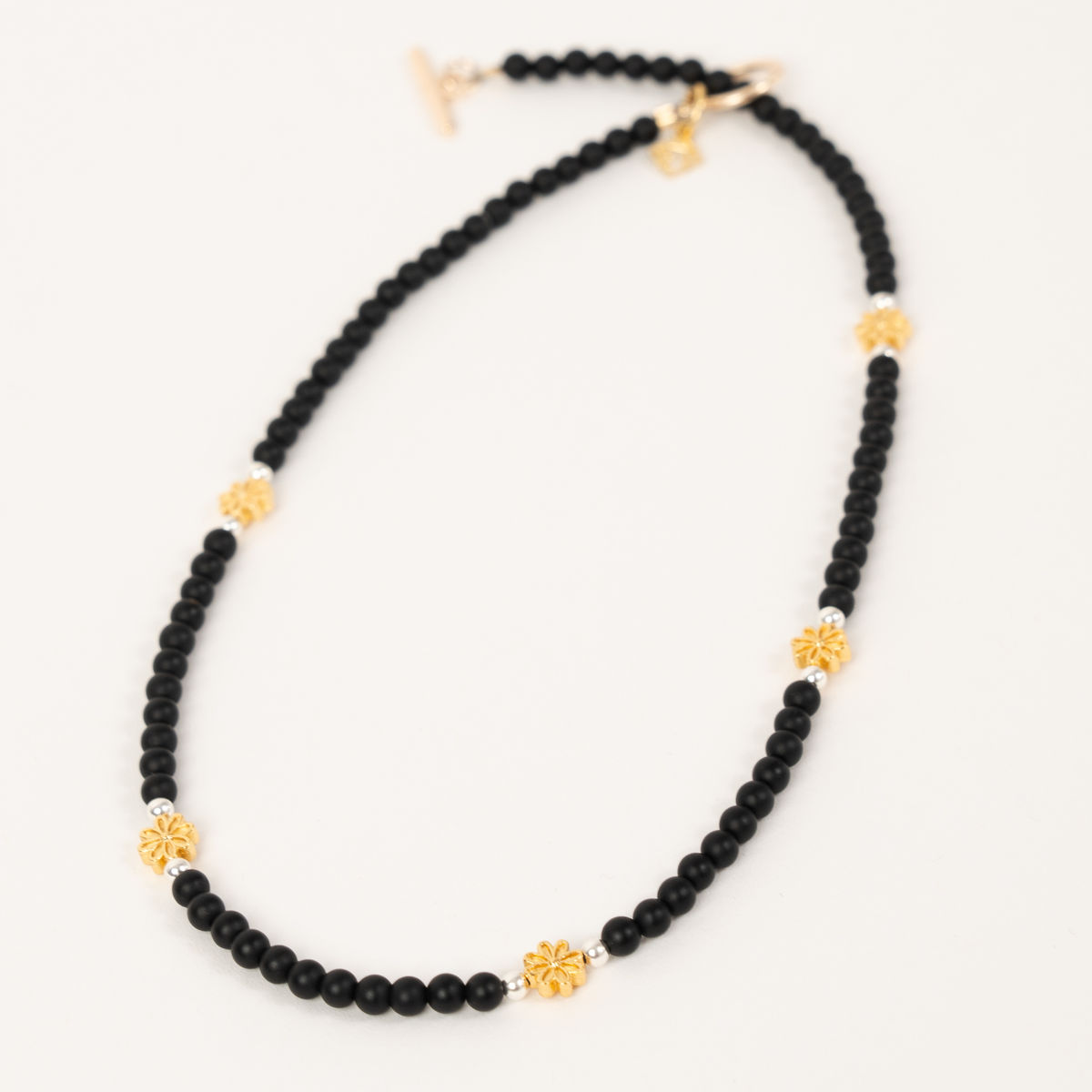 Petite Fleur necklace with matte black beads, golden flower accents and a signature ER charm