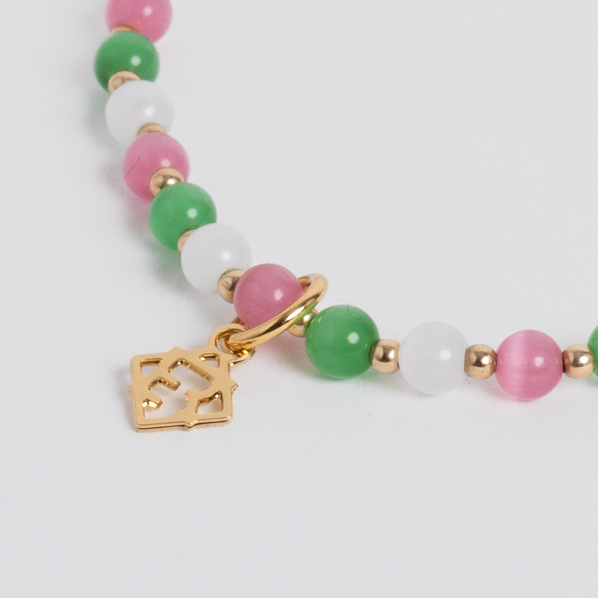 Close-up of pink, green and white cat’s-eye stones with 14K gold-filled beads and a golden ER charm