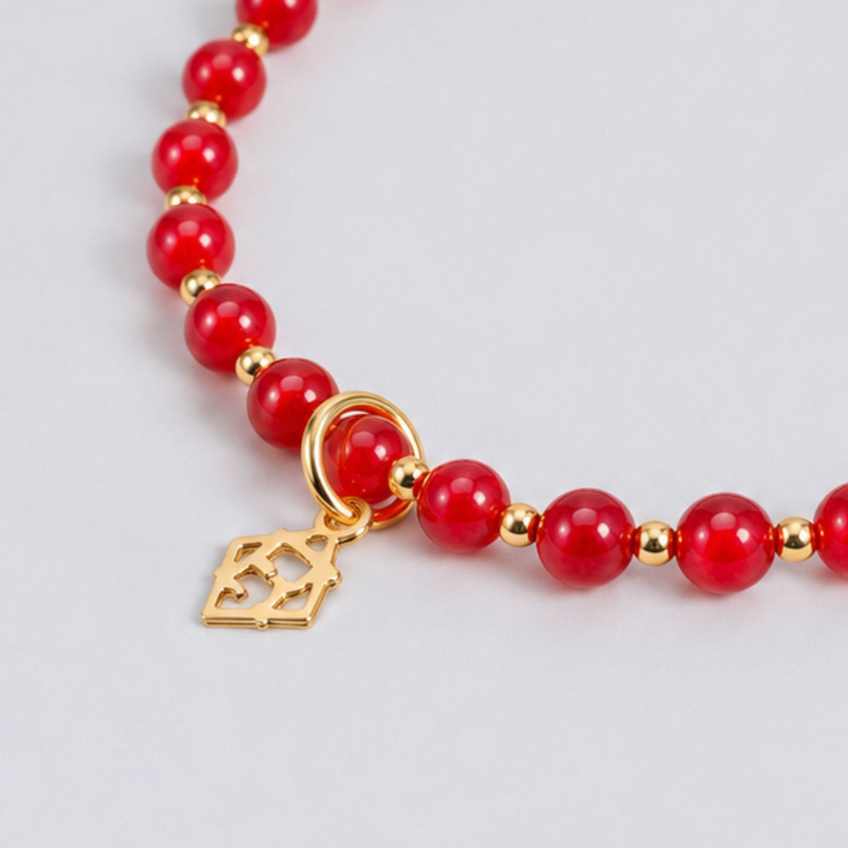 Close-up of the red cat’s-eye beads, 14K gold-filled accents and ElyseRyan charm on the Prism Apple Red Bracelet