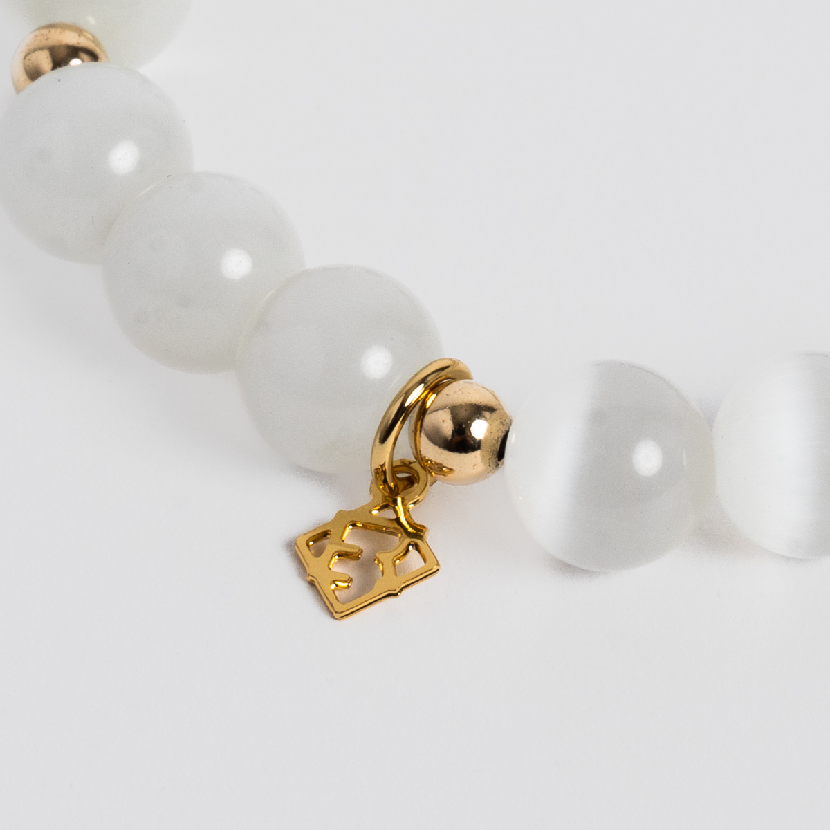 Close-up of the Prism Maxi Cloud White Bracelet with luminous white cat’s-eye beads, 14K gold-filled spacers and a signature golden ER charm
