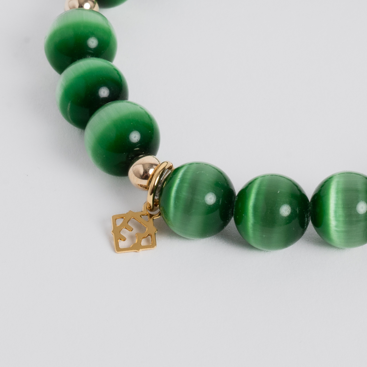 Close-up of the Prism Maxi Evergreen Bracelet with green cat’s-eye beads, gold-filled accents and a golden ER charm