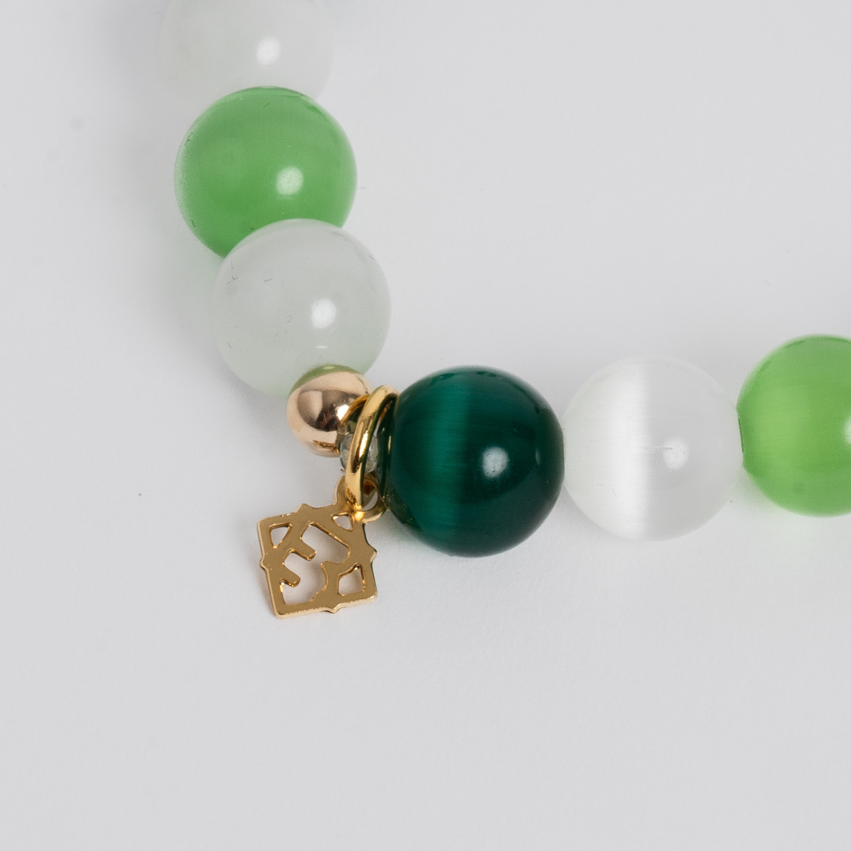 Close-up of the Prism Maxi Multi Greens Bracelet with lime, white and evergreen cat’s-eye beads and a golden ER charm