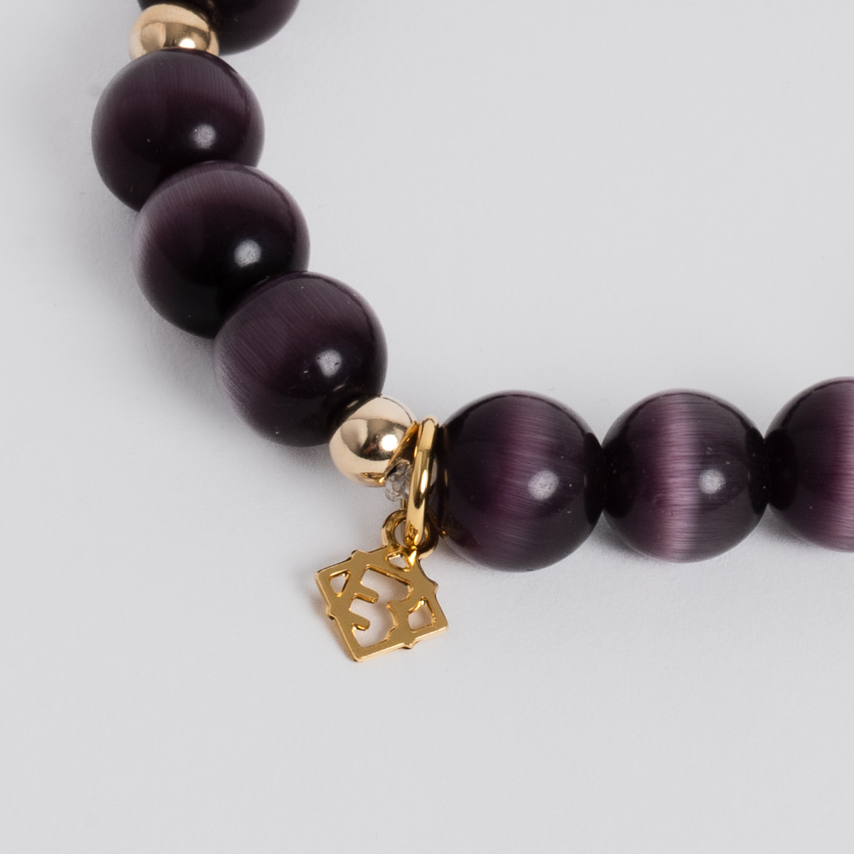 Close-up of the Prism Maxi Plum Bracelet with dark purple cat’s-eye beads, 14K gold-filled spacers and a signature golden ER charm