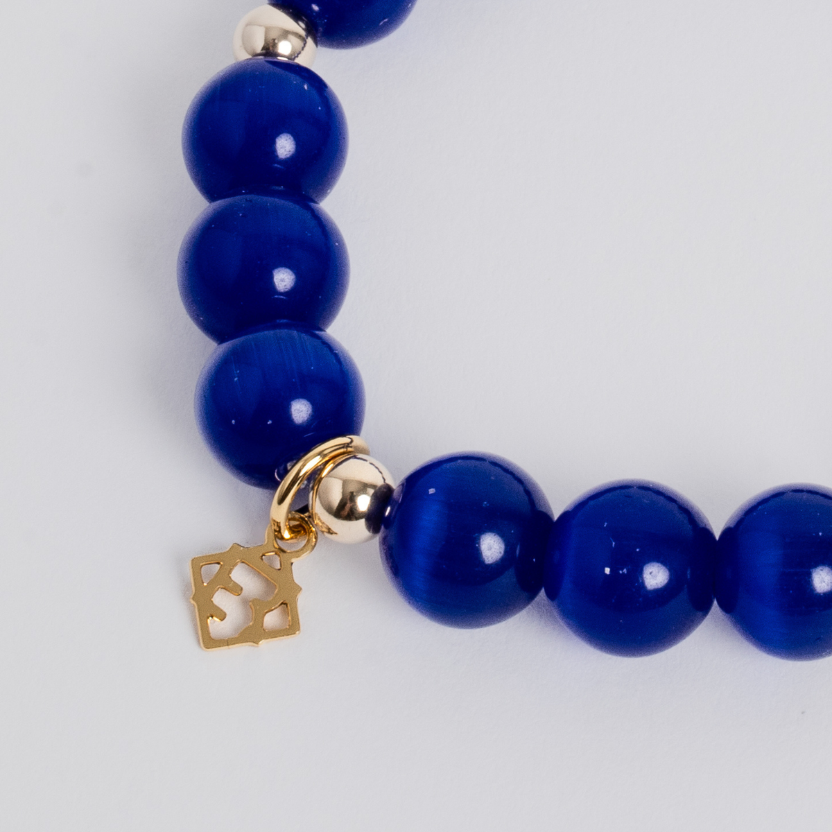 Close-up of the Prism Maxi Royal Blue Bracelet with luminous cat’s-eye beads, 14K gold-filled spacers and a signature golden ER charm