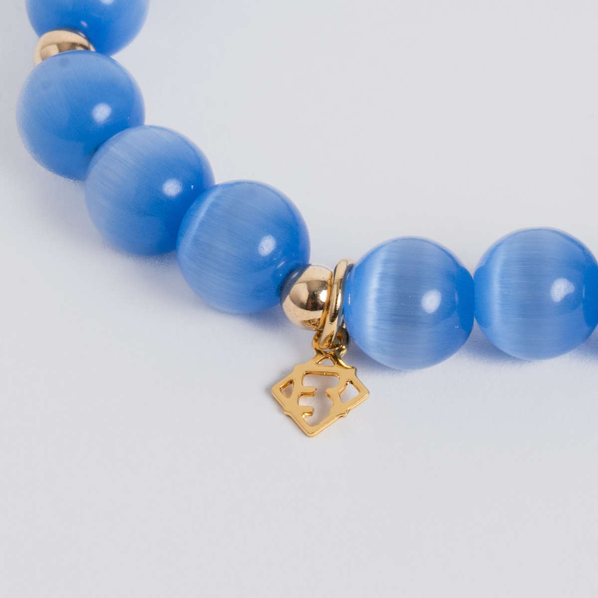 Close-up of the Prism Maxi Sky Blue Bracelet with luminous cat’s-eye beads, 14K gold-filled spacers and a signature golden ER charm