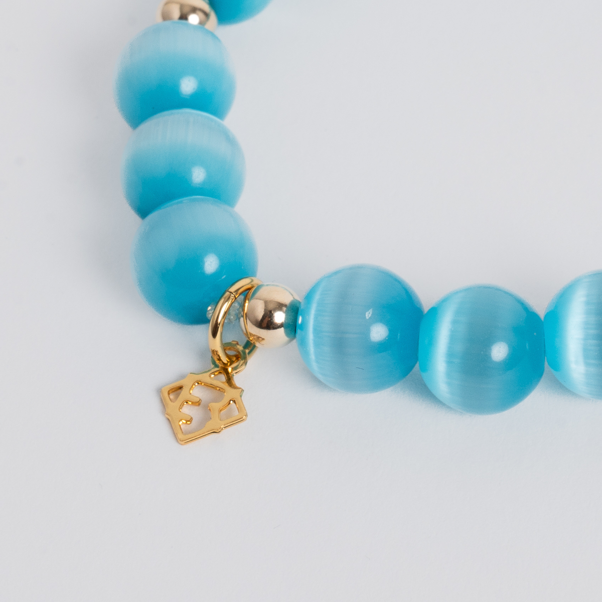 Close-up of the Prism Maxi Turquoise Blue Bracelet with luminous cat’s-eye beads, 14K gold-filled spacers and a signature golden ER charm