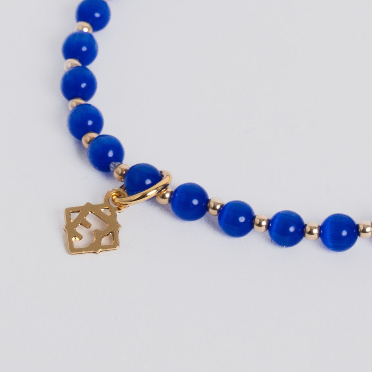 Close-up of the Prism Royal Blue Bracelet with luminous cat’s-eye beads, 14K gold-filled spacers and a signature golden ER charm