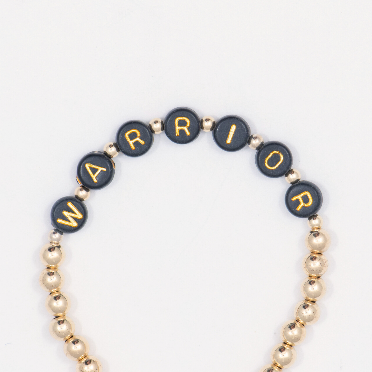 Close-up of black letter beads spelling WARRIOR on the 14K gold-filled Thoughtful bracelet