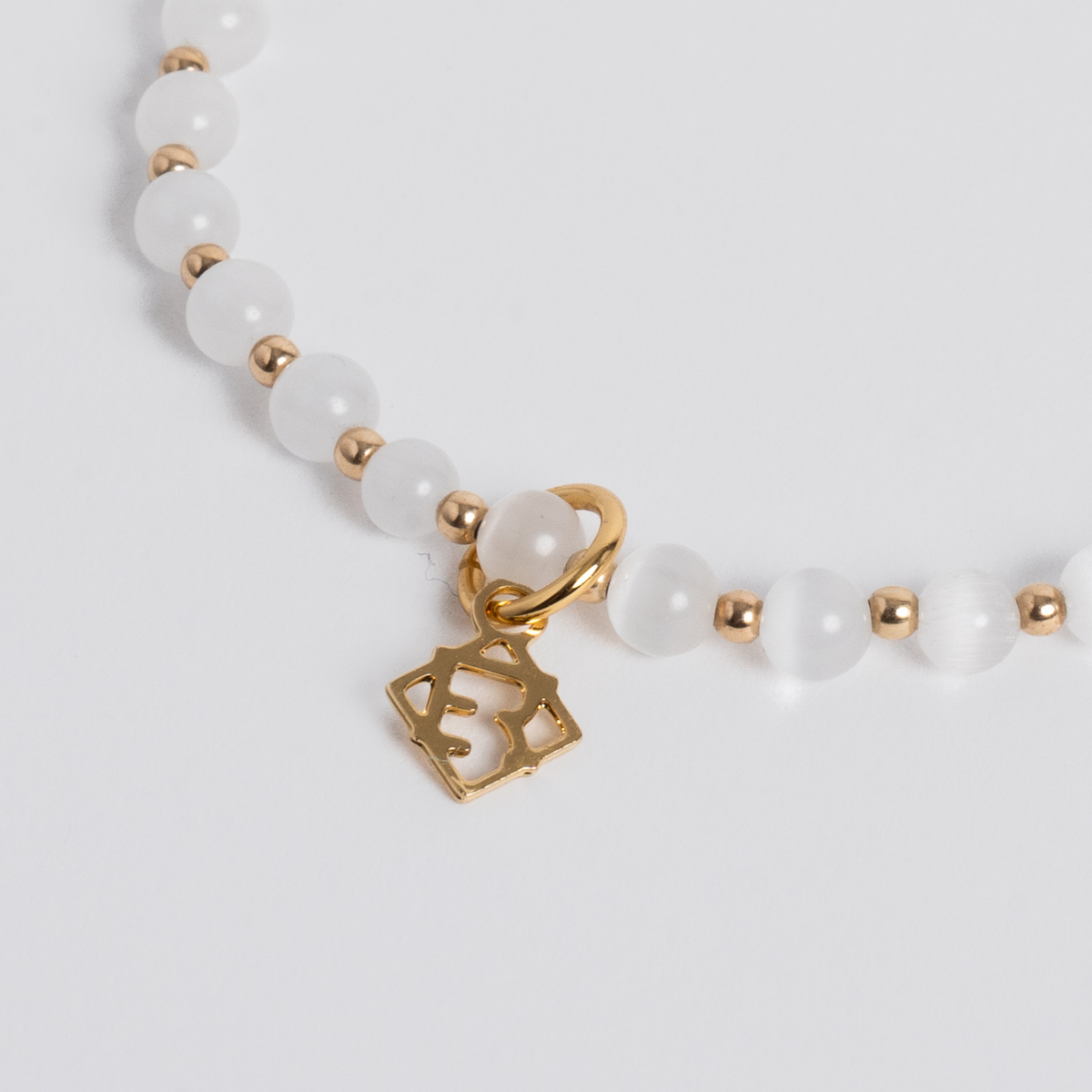 Close-up of luminous white cat’s-eye stones with 14K gold-filled beads and a golden ER charm