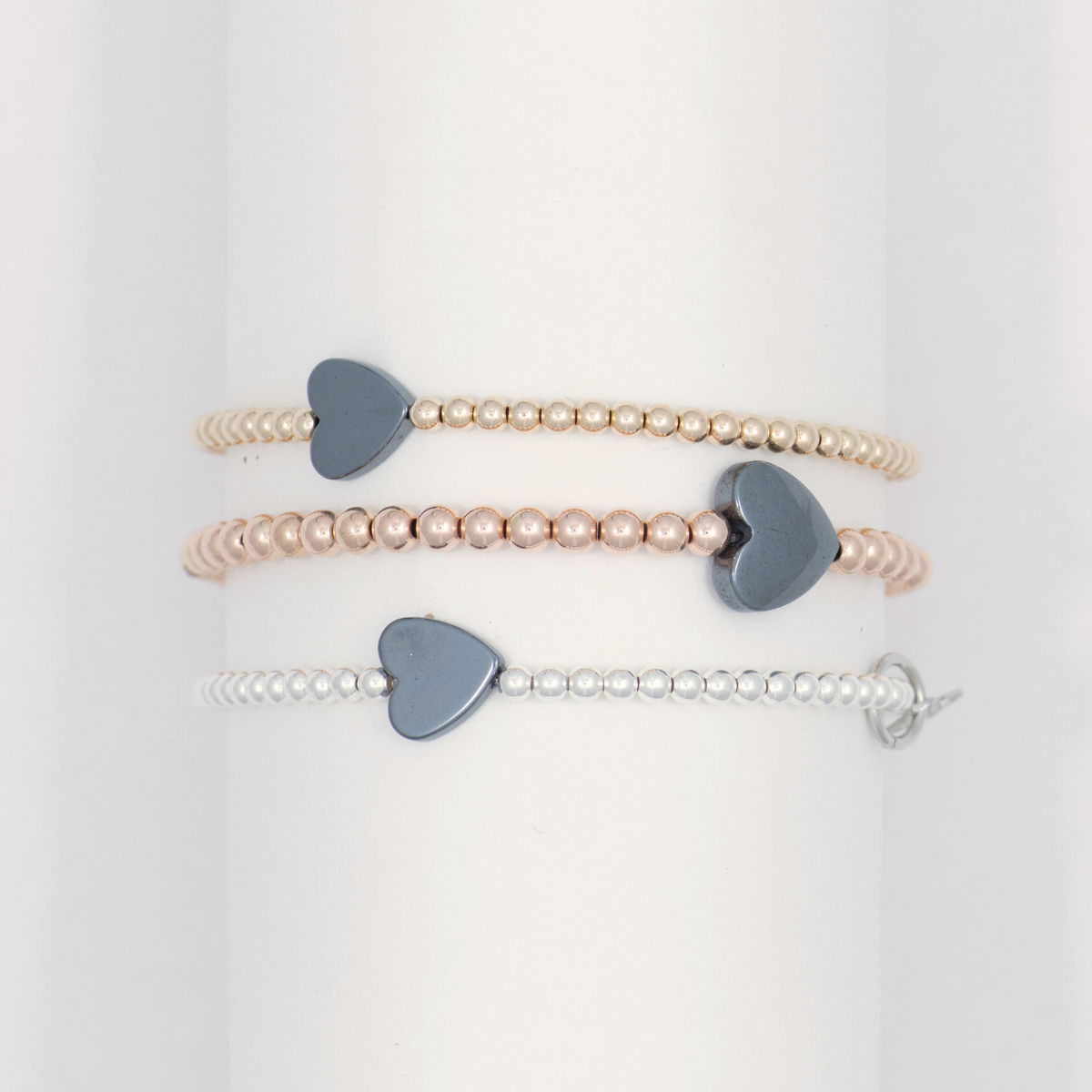 Three Happy Heart bracelets in gold, sterling silver and rose gold finishes, each with a dark hematite heart