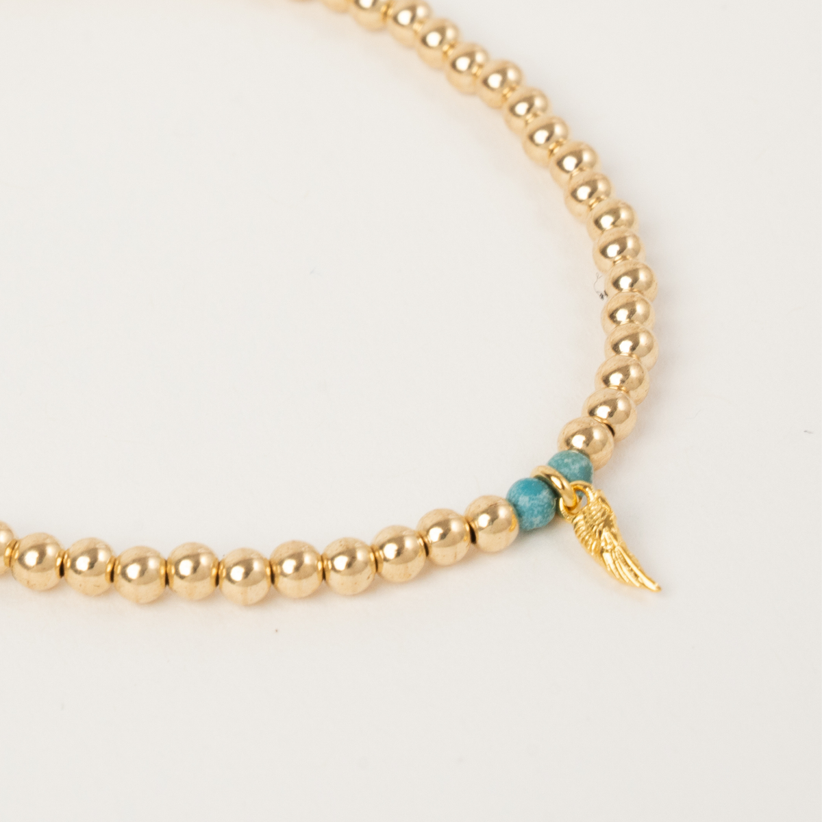 Close-up of turquoise gemstone beads and the golden angel wing on the Haven memorial bracelet