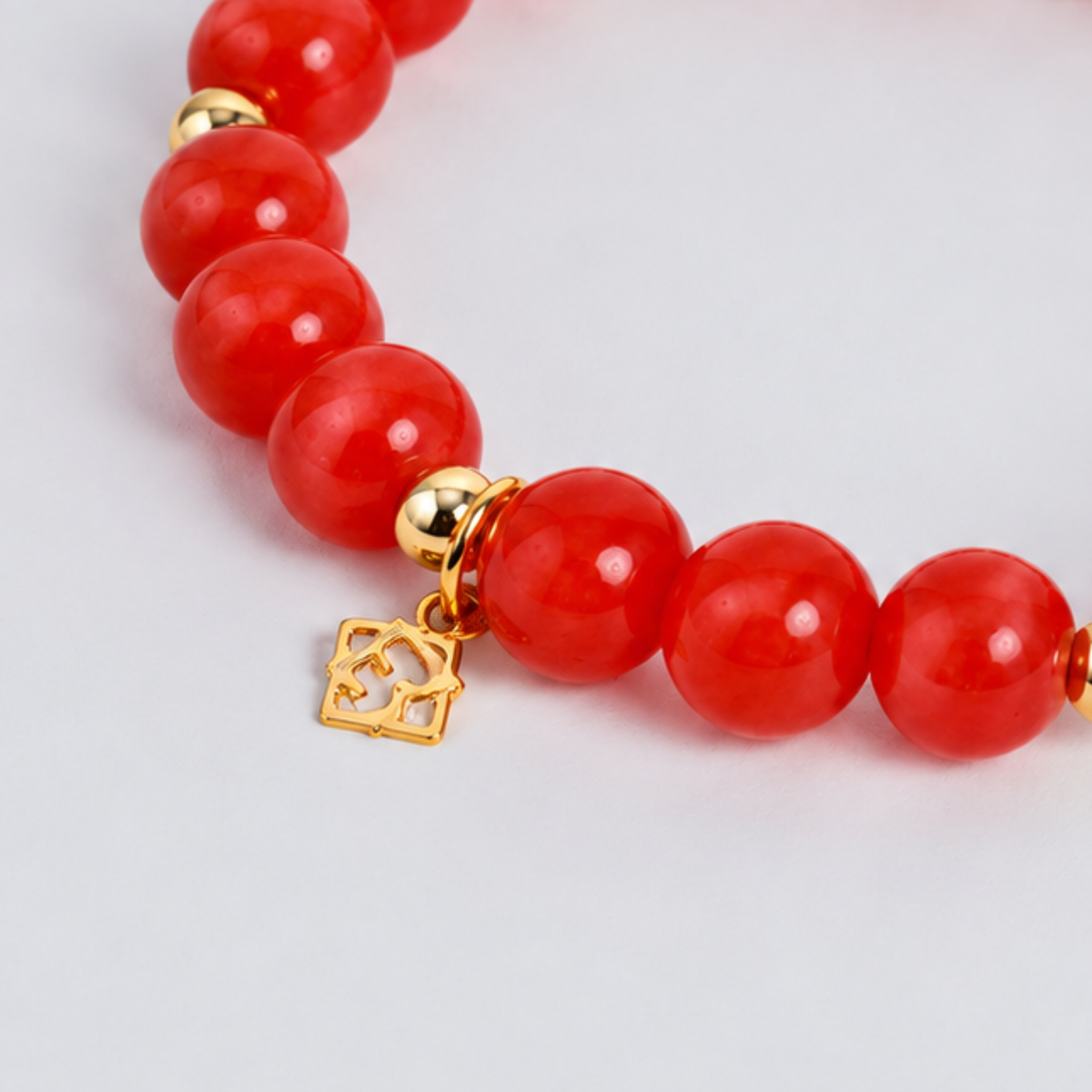 Close-up of the Prism Maxi Apple Red Bracelet with luminous red cat’s-eye beads, 14K gold-filled spacers and a signature golden ER charm