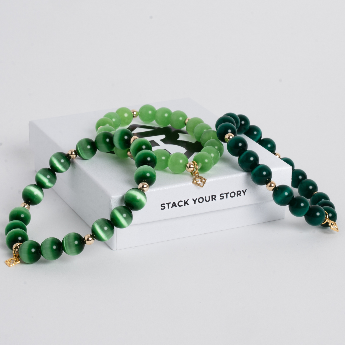 Three Prism Maxi cat's eye bracelets in Evergreen, Lime Green and Deep Green with gold-filled accents, displayed on ElyseRyan jewelry packaging