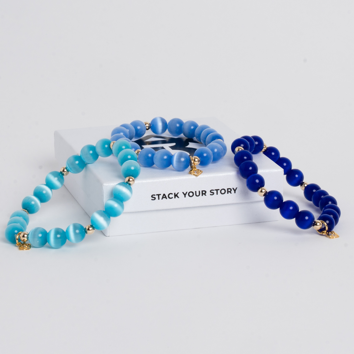 Three Prism Maxi cat's eye bracelets in Royal Blue, Turquoise Blue and Sky Blue with gold-filled accents, displayed on ElyseRyan jewelry packaging