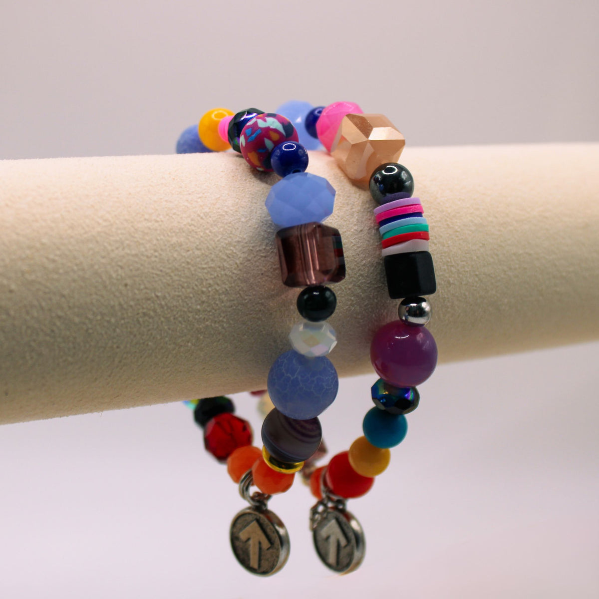 Two colorful SU2C WristRock bracelets with mixed beads and arrow charms on a display stand