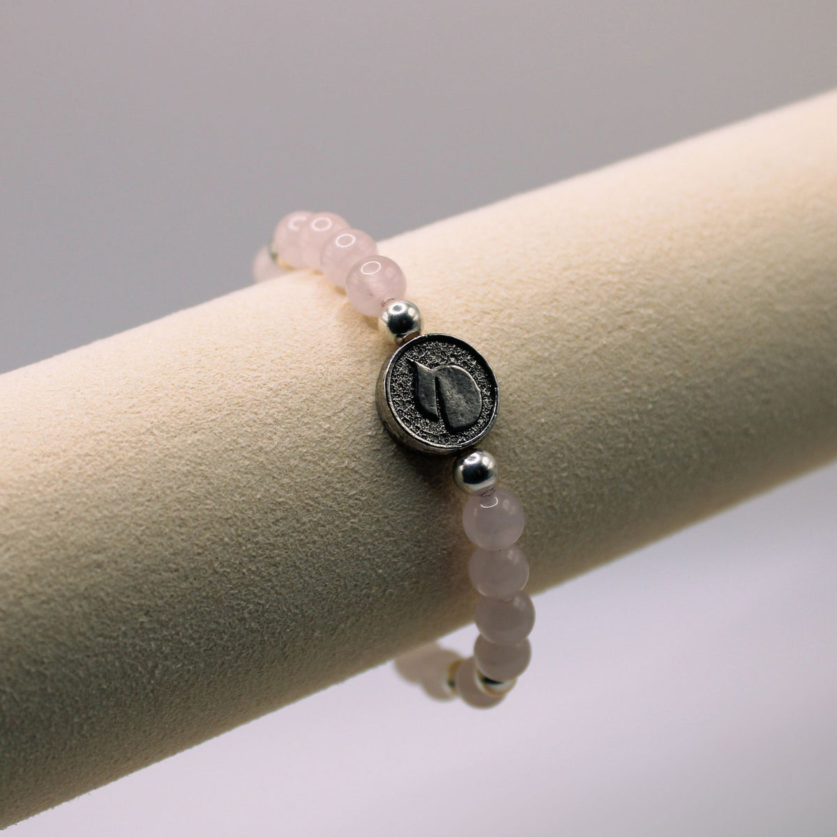 Win with Love bracelet with pale pink beads, silver accents and a round centerpiece on a display stand