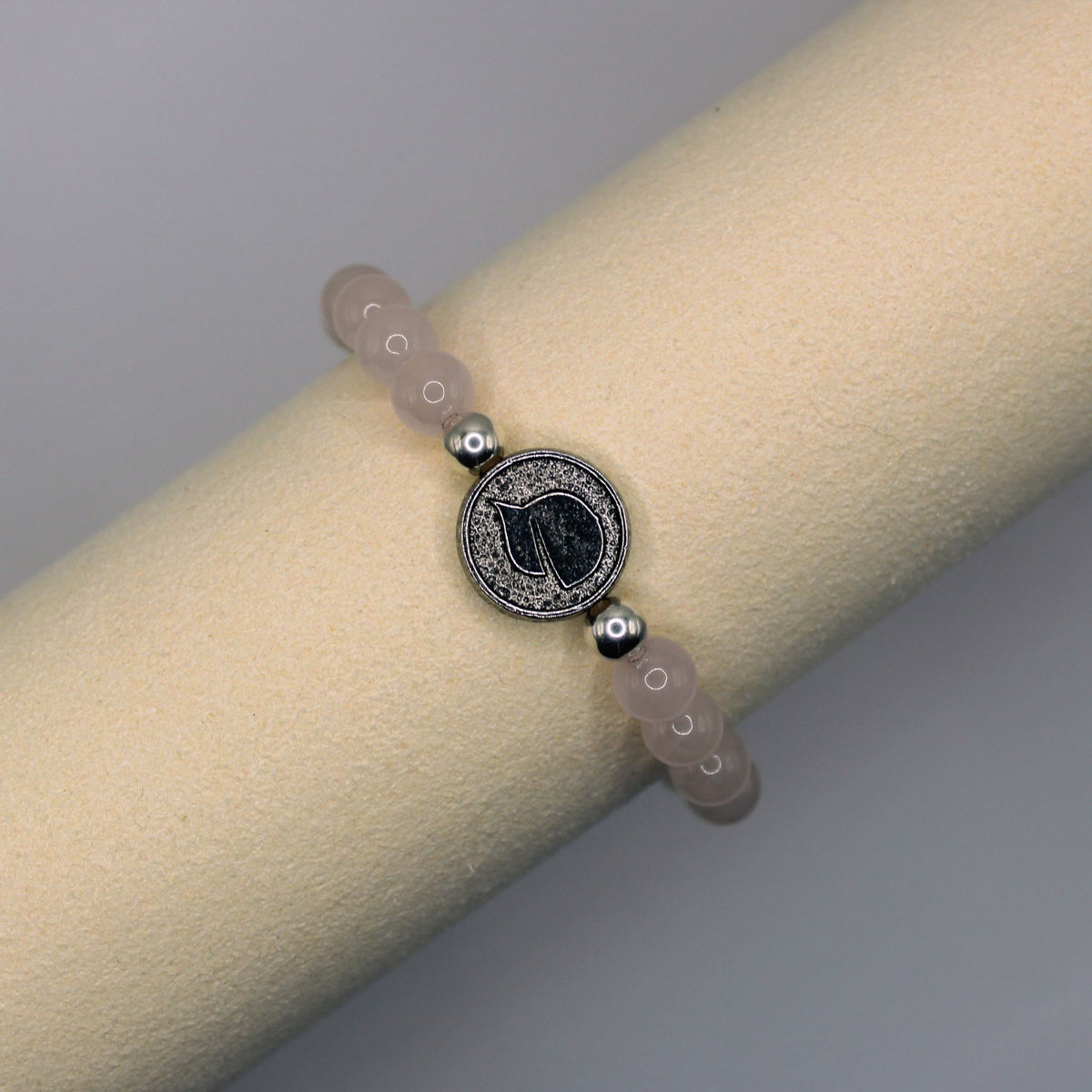 Close view of the Win with Love bracelet’s round silver-toned centerpiece and pale pink beads